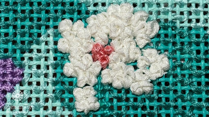Silk ribbon French knots form the petals of this white flower.