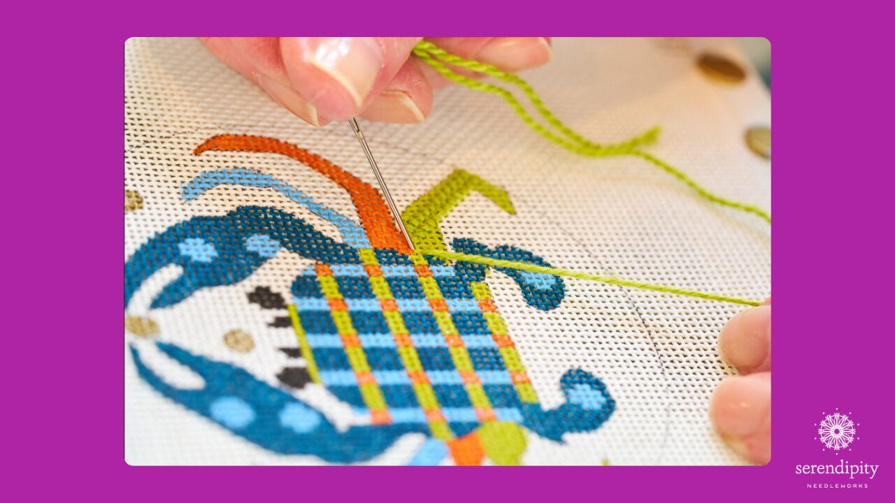 Close-up of Ellen Johnson stitching a painted needlepoint canvas of a Melissa Prince Designs crab with various decorative stitches in progress
